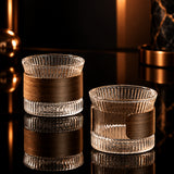 Two glass candle holders with wooden bases on a wooden surface.