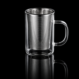 Glass mug with metal tea infuser being filled with tea leaves, on a gray surface.