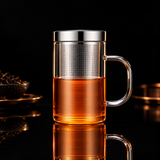 Glass mug with metal mesh tea infuser and lid on a wooden surface, featuring KEMORELA branding.