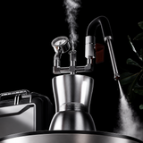 A stainless steel steam boiler coffee maker with a curved steam spout and built-in pressure gauge, shown with steam rising and promotional text on a dark gray textured background.