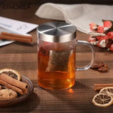 Glass mug with tea and cinnamon sticks on a wooden surface, featuring KEMORELA branding.
