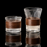 Two clear glass cups with brown leather bands on a textured surface.