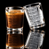 Two clear glass measuring cups with printed espresso and coffee strength markings, shown on a white background. One cup is filled with tan coffee and the other is empty.
