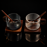 Two glass cups with wooden stirrers on wooden coasters against a white background.